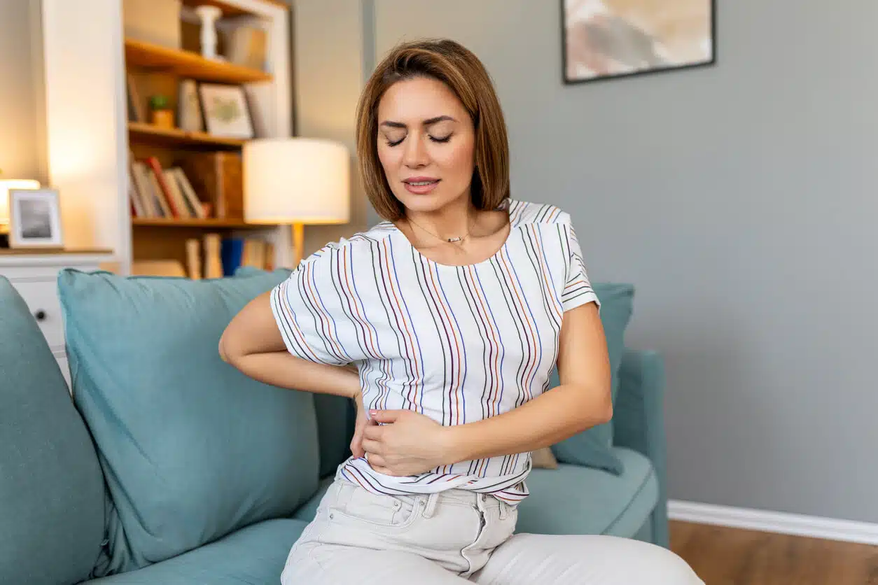 A close-up image of a young woman with lower back pain, causing her to hold her lower back.